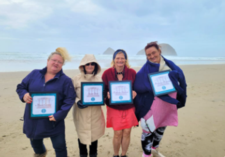 Four women holding up ipads on the beach.